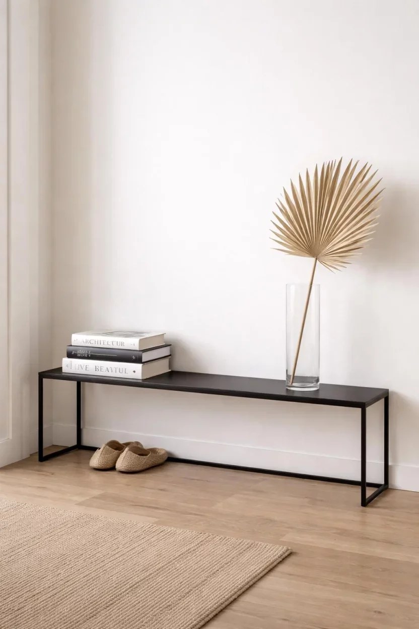 Minimalist black steel bench with decorative dried palm leaf vase.