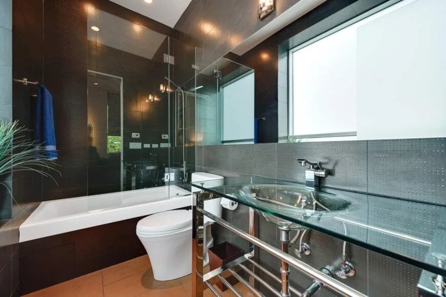 Luxurious dark bathroom with glass sink and bathtub combination.